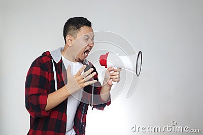 Portrait of funny young Asian man shouting with megaphone, mad yelling screaming crazy supporting motivating Stock Photo