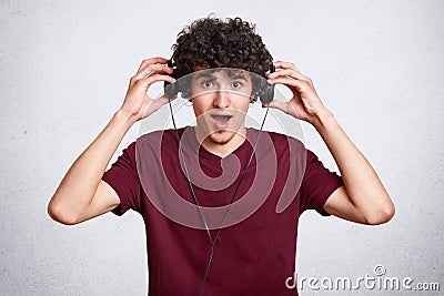 Portrait of funny young man with awesome hairdo. Attractive teenager with opened mouth listens to favourite songs with headphones Stock Photo