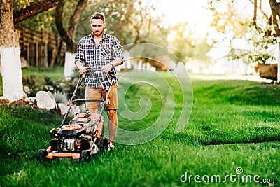 Portrait of young gardener using lawn mower for grass cutting in garden Stock Photo