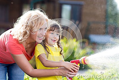 Portrait of gardener woman with daughter watering flowers on the lawn near cottage. Stock Photo