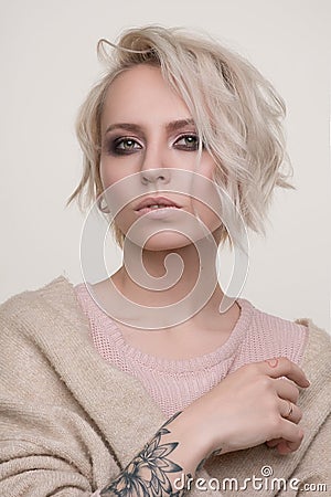 Portrait of girl of blonde with dark eye makeup and short hair in a light pink sweater standing on a light background looking into Stock Photo