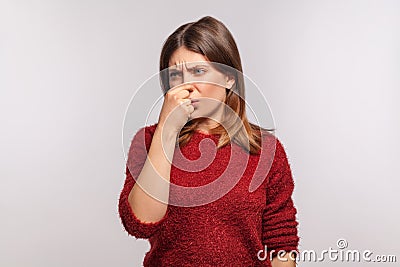 Portrait of girl in shaggy sweater grimacing in disgust and pinching her nose, confused by bad breath, stinky Stock Photo