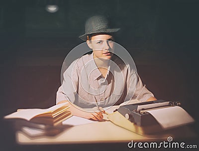 Portrait of a girl sitting at a table with a typewriter and books, think about the idea at night Stock Photo