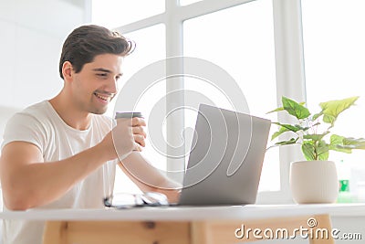 Portrait of handsome man sitting at table at home with laptop computer, smiling at camera Stock Photo