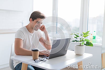 Portrait of handsome man sitting at table at home with laptop computer, smiling at camera Stock Photo