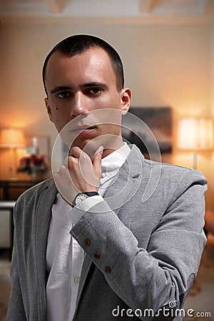 Portrait of goodlooking thoughtful young businessman in gray jacket and white t-shirt, looking at camera Stock Photo