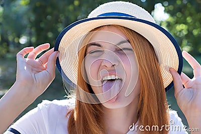 Portrait of gorgeous teenage girl in yellow hat and with red hair showing her tongue outdoors on sunny summer day Stock Photo