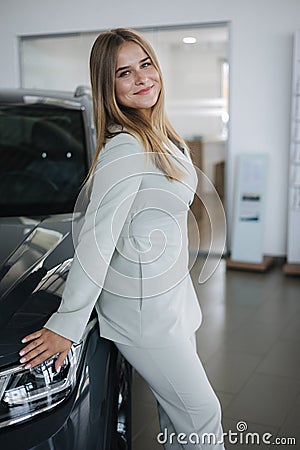 Portrait of gorgeous woman in showroom. Beautiful salesperson standing by car. Blond hair female after buying car Stock Photo