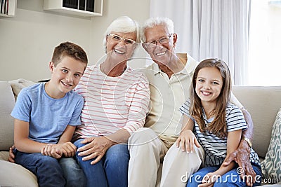 Portrait Of Grandchildren Sitting On Sofa With Grandparents Stock Photo