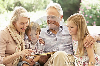 Portrait Of Grandparents Reading To Grandchildren On Sofa Stock Photo