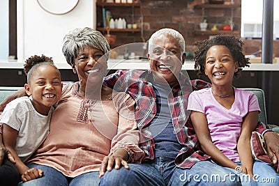 Portrait Of Grandparents Sitting On Sofa At Home With Granddaughters Stock Photo