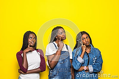 Portrait of group of three beautiful african women with hand on chin thinking about question, pensive expression over yellow Stock Photo