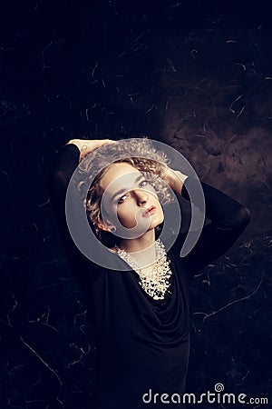 A portrait of guy androgyne model with blond hair posing sitting in a black dress on a dark background in the image of a woman Stock Photo