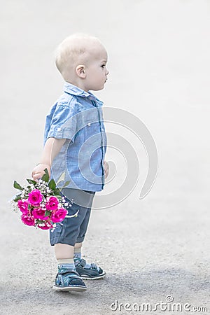 Portrait half-face of small baby boy standing with pink roses bouquet outdoor. Little gentleman with flowers looking to Stock Photo