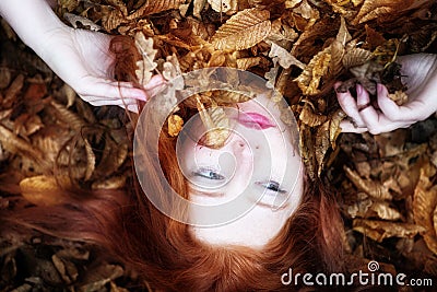 Portrait and hands of a natural young lady, covered with red and orange autumnal leaves. Beautiful woman lying Stock Photo