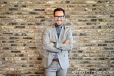 Portrait of handsome accountant with arms crossed and in eyeglasses standing by brick wall in office Stock Photo