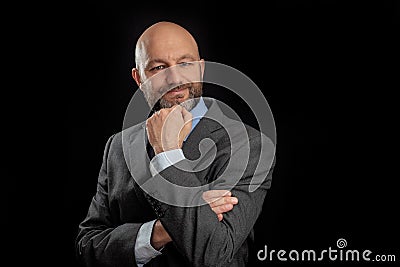 Portrait of a handsome bald businessmen in grey suit on black background. The model is in his 40s, shaven head and grey and dark Stock Photo