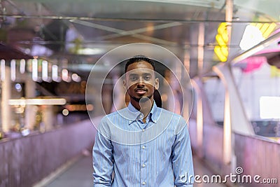 Portrait of handsome black African businessman outdoors in city at night standing at footbridge Stock Photo