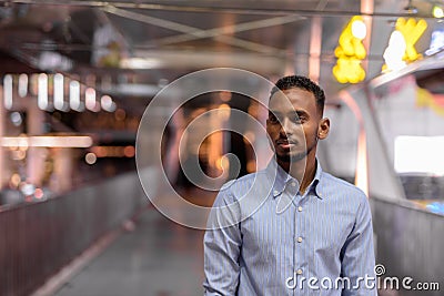 Portrait of handsome black African businessman outdoors in city at night standing at footbridge Stock Photo