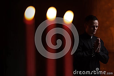 Portrait of handsome catholic priest or pastor with dog collar, dark red background. Stock Photo