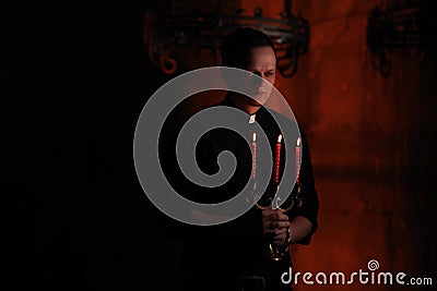 Portrait of handsome catholic priest or pastor with dog collar, dark red background. with three red candle in the hand Stock Photo