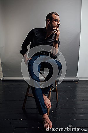 Portrait handsome fashionable man in a black shirt sits on a chair in a photo studio loft. Stock Photo