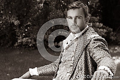 Portrait of handsome gentleman dressed in vintage costume sitting on bench in garden Stock Photo