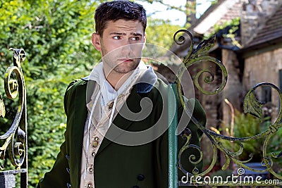 Portrait of handsome gentleman dressed in vintage costume standing next to iron gate with courtyard in background Stock Photo