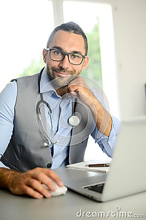 Portrait of handsome man male doctor in medical practice office writing prescription in laptop computer Stock Photo