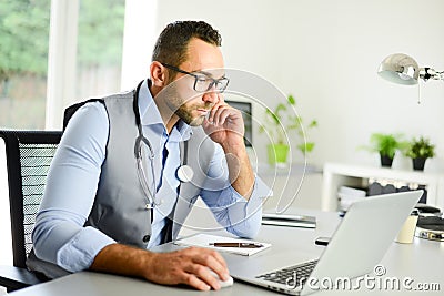 Portrait of handsome man male doctor in medical practice office writing prescription in laptop computer Stock Photo