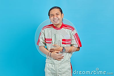 Portrait of handsome man wearing mechanic uniform loughing hard out loud because funny crazy joke with hands on body Stock Photo