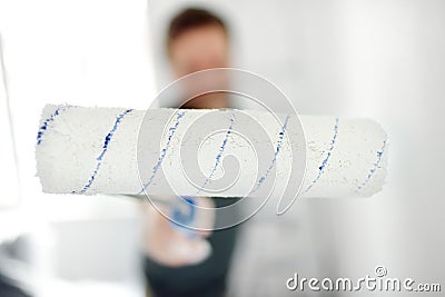 Portrait of a handsome mature man making repairs in the apartment. The person paints the wall white with roller. Do it yourself. Stock Photo