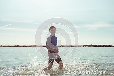 Portrait of handsome teen boy running in neoprene swimsuit in sea Stock Photo