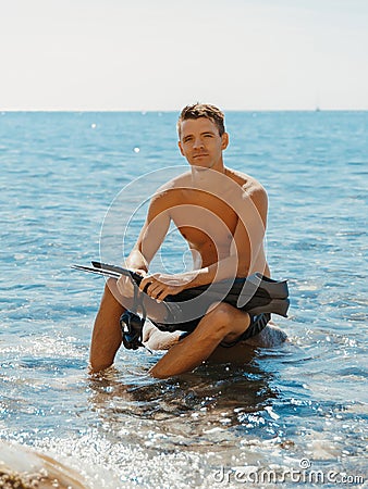 Portrait of handsome topless male model on the sea beach. Sporty man sit on the stone with diving fins and mask Stock Photo