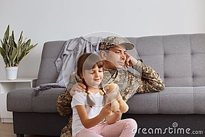 Portrait of handsome young adult soldier man wearing camouflage uniform returning home after army, spending time with daughter, Stock Photo