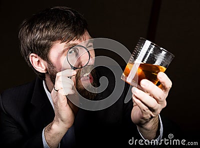 Portrait of handsome young businessman looking at brandy through magnifying glass Stock Photo