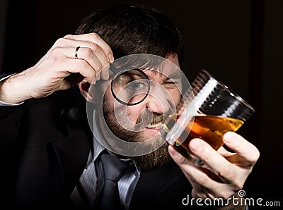 Portrait of handsome young businessman looking at brandy through magnifying glass Stock Photo