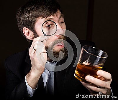 Portrait of handsome young businessman looking at brandy through magnifying glass Stock Photo