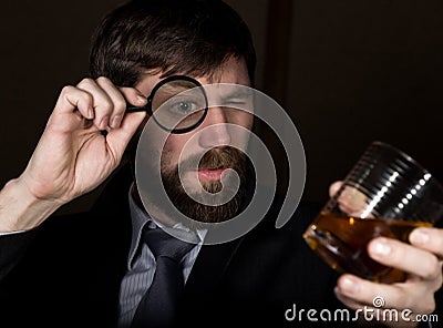 Portrait of handsome young businessman looking at brandy through magnifying glass Stock Photo