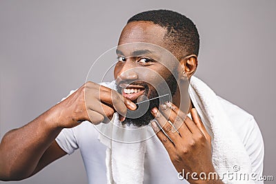 Portrait of handsome young african american black man combing his beard in bathroom. Isolated over grey background Stock Photo