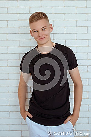 Portrait of hansome young man teen in black t-shirt and white pants on white bricks Stock Photo
