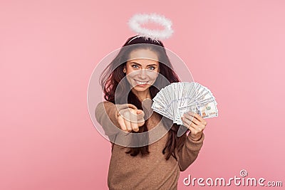 Portrait of happy angelic young woman with halo above head holding dollar banknotes and pointing to camera Stock Photo