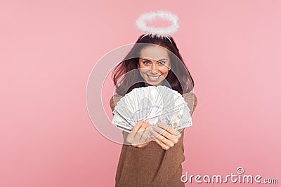 Portrait of happy angelic young woman with halo above head holding dollar banknotes, showing big money Stock Photo
