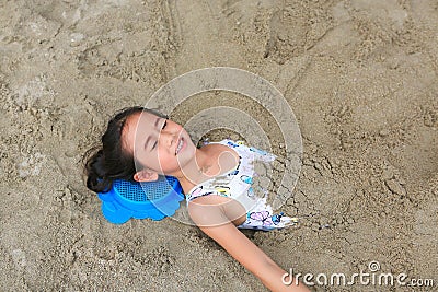 Portrait of happy asian little child girl buried in the sand at the beach. Close up kid playing with sand Stock Photo