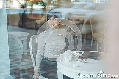 Portrait of happy attractive smiling woman with shor hair wearing sitting in cafe looking through a window, view through Stock Photo