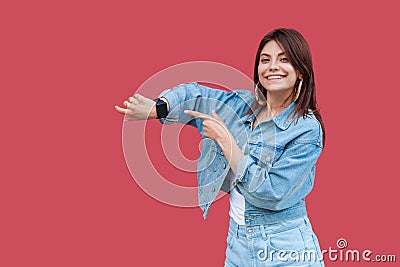 Portrait of happy beautiful brunette young woman with makeup in denim casual style standing showing and pointing at her smart Stock Photo