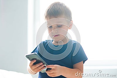 Portrait of happy boy playing with a smartphone. Kid with a mobile phone at home. Entertainment technology, futuristic Stock Photo