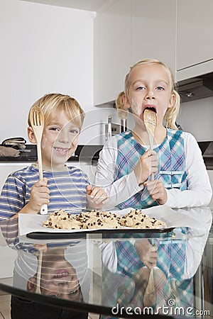 Portrait of happy boy with sister tasting spatula mix with cookie batter in kitchen Stock Photo