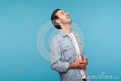 Portrait of happy carefree man in worker denim shirt laughing out loud and holding belly, chuckling Stock Photo