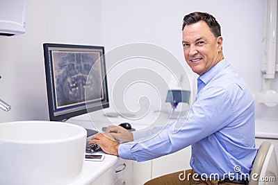 Portrait of happy dentist examining x-ray report on computer Stock Photo